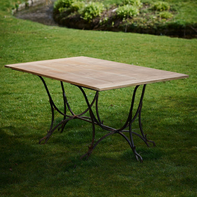 Wrought iron and teak garden table standing plainly on a summer lawn