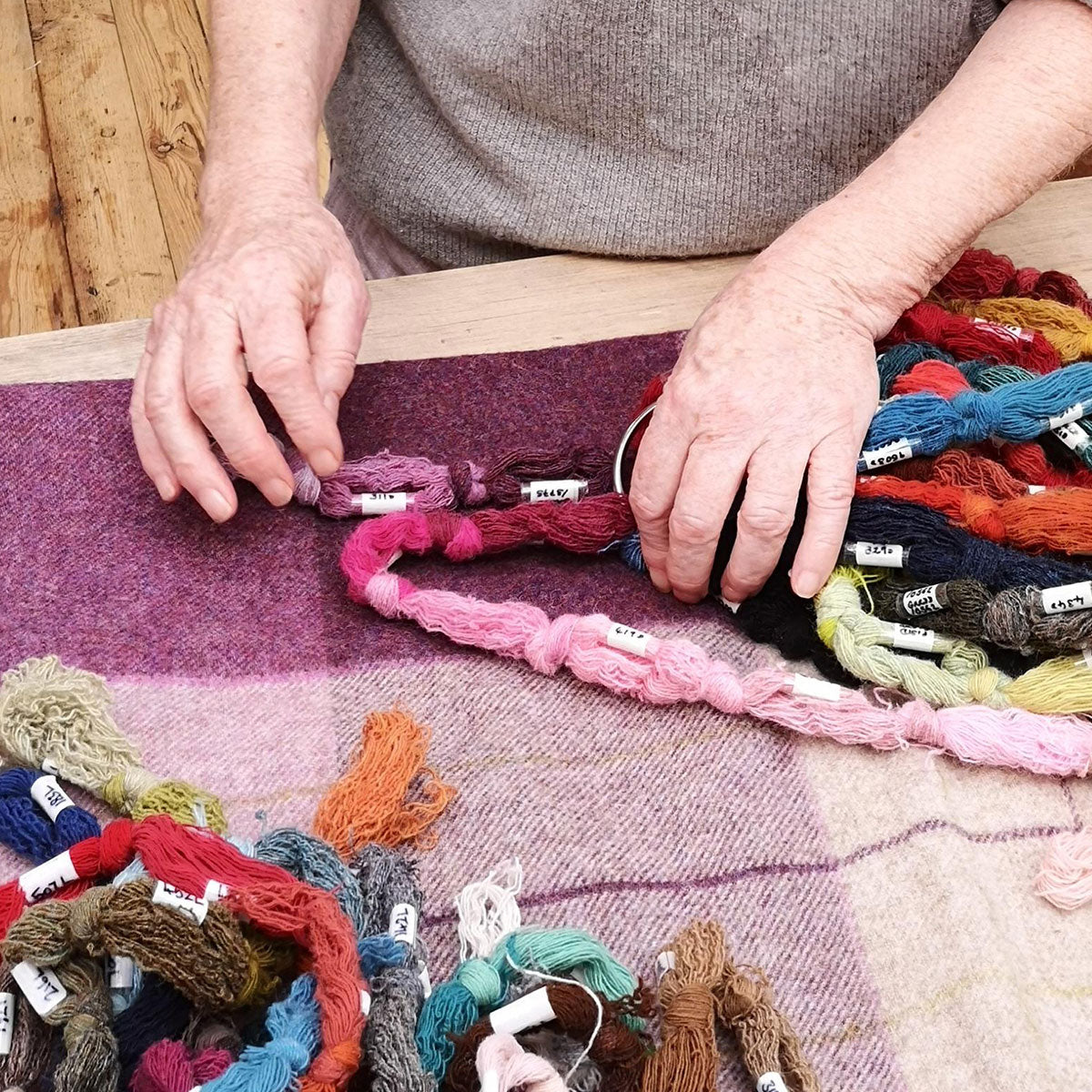 Weaver's hands finishing the throw's fringe among coloured yarns