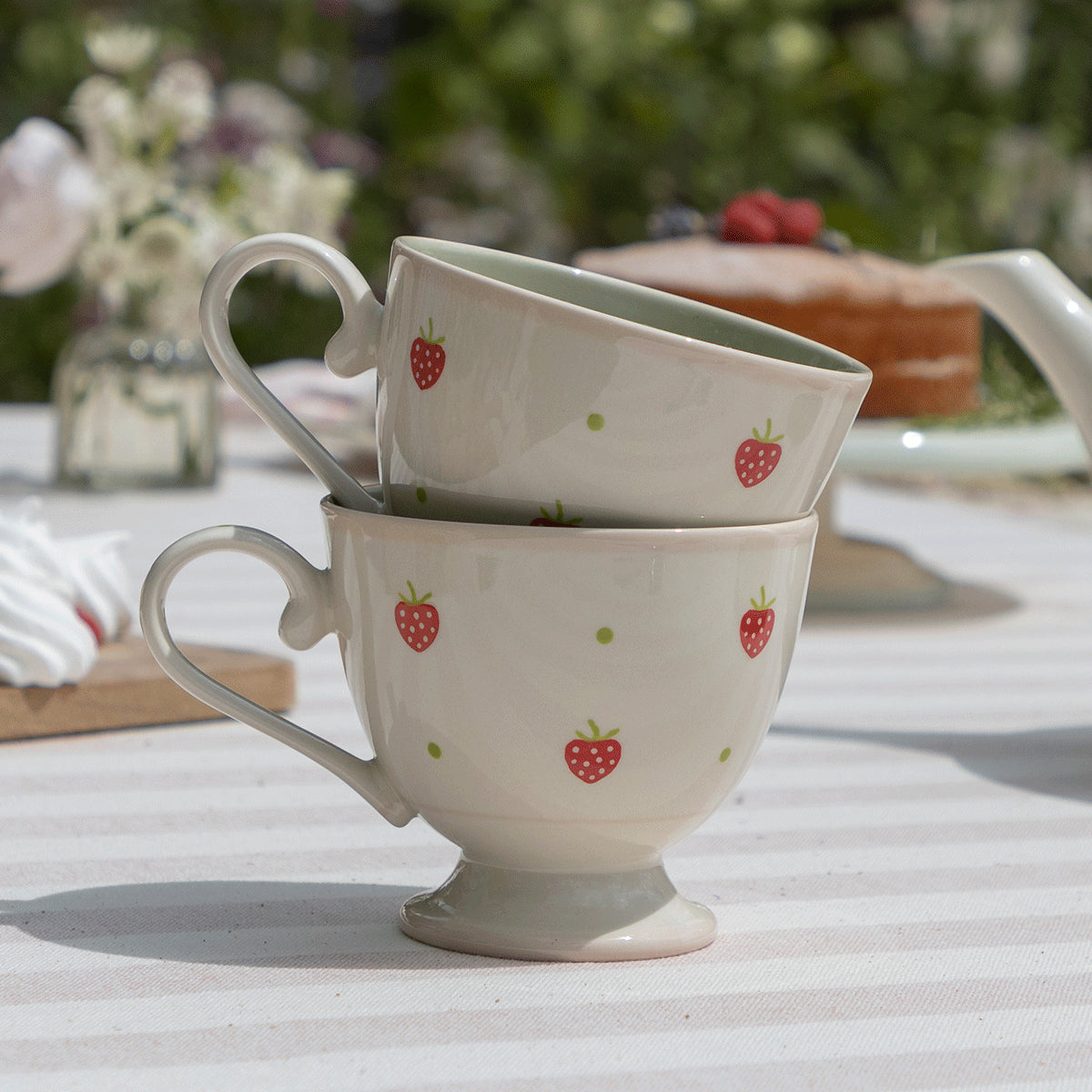 Stacked strawberry mugs beside a jug of white blossom