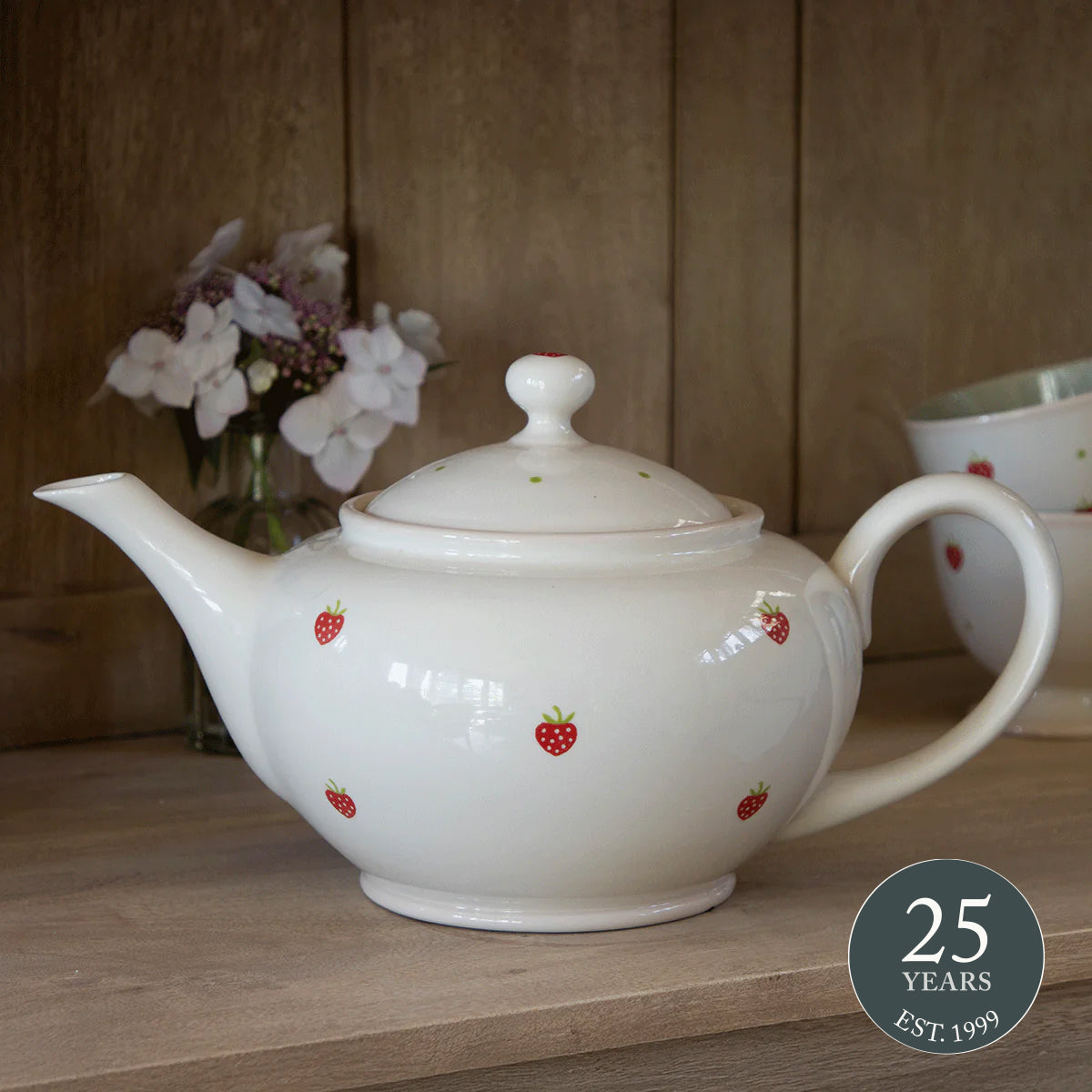 Strawberry giant teapot on a wooden table with white orchids