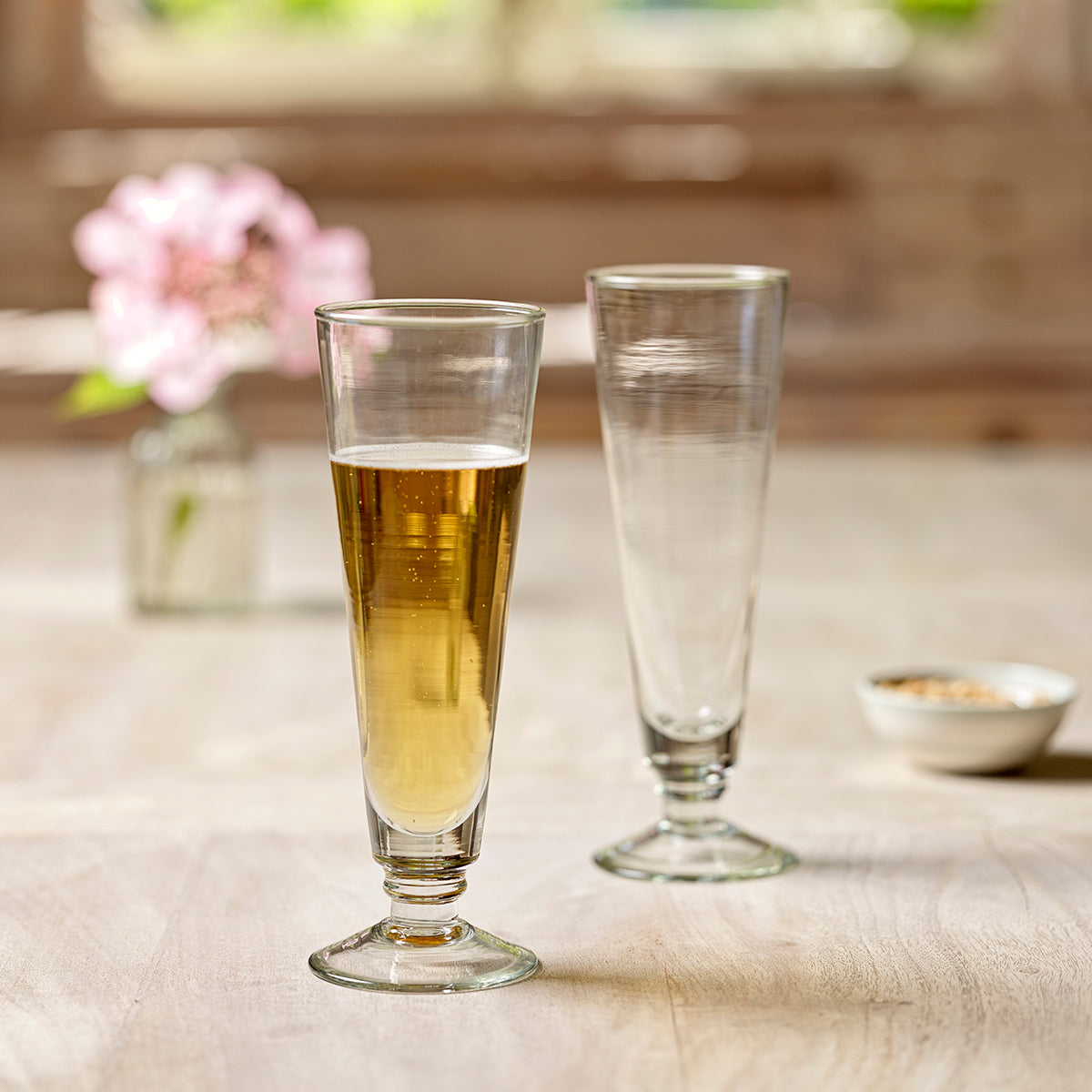 Two hand-blown beer glasses, one filled, beside a posy indoors