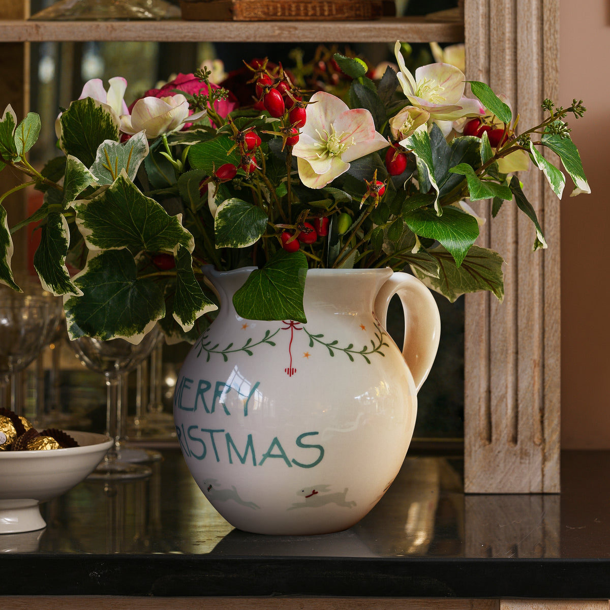 Merry Christmas jug of festive foliage in a candlelit room