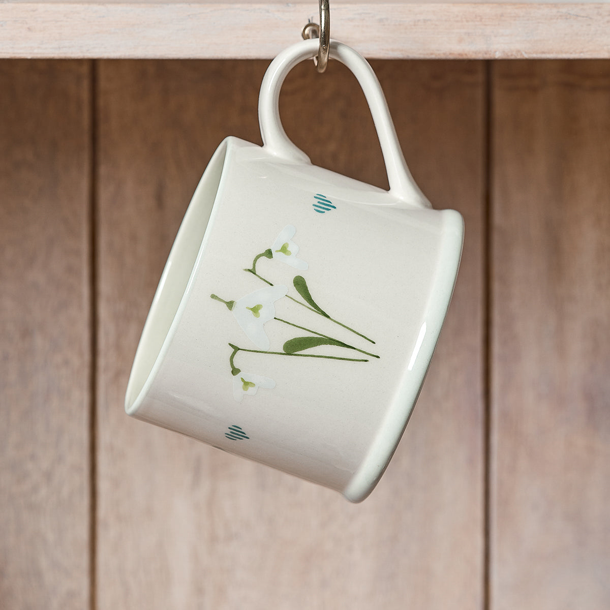 Snowdrop straight mug hanging from a hook on wooden panelling