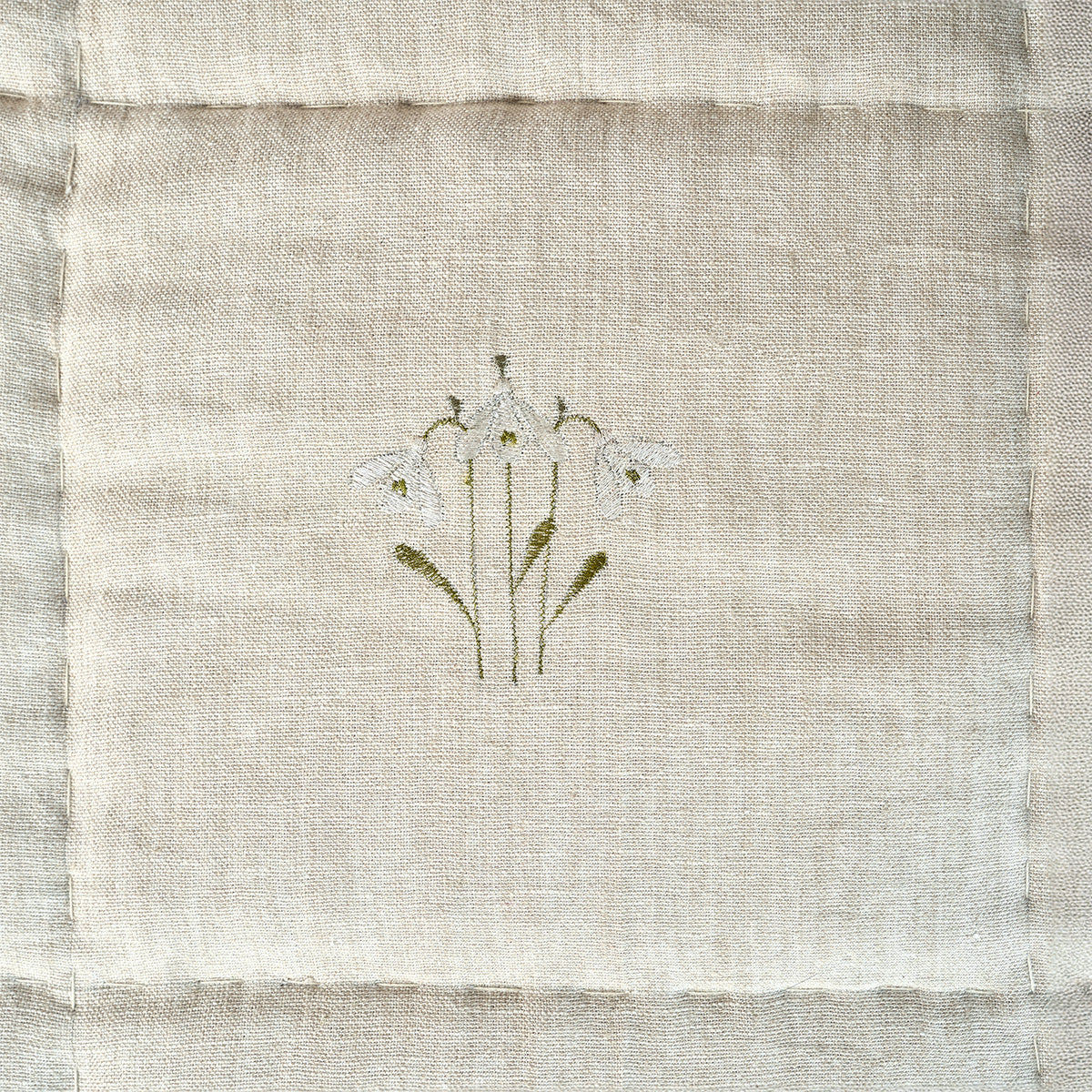 Close view of a single embroidered snowdrop sprig on the quilted linen