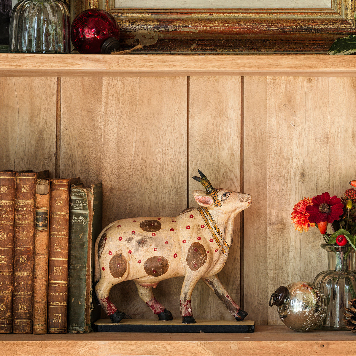 Hand-carved wooden cow painted with red spots, beside old books