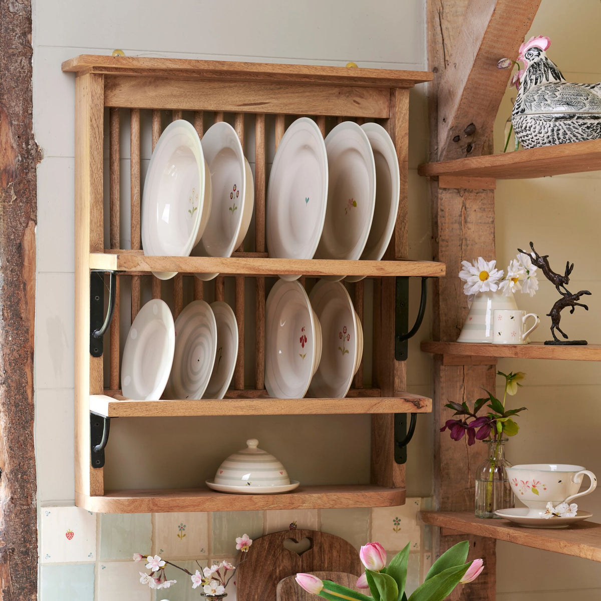 Wooden plate rack holding white plates, cups and jugs on a kitchen wall