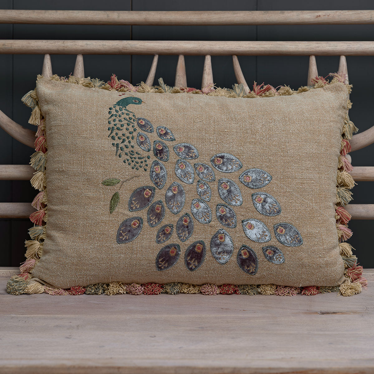 Embroidered peacock cushion on saffron linen with tassel trim, on a bench