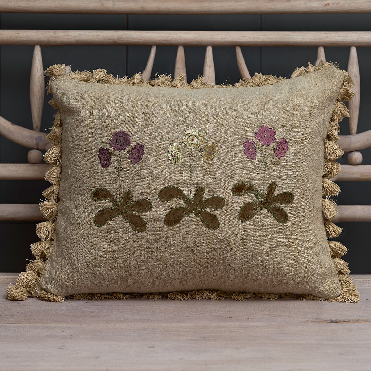 Embroidered Golden Auriculas linen cushion with tassel trim on a bench