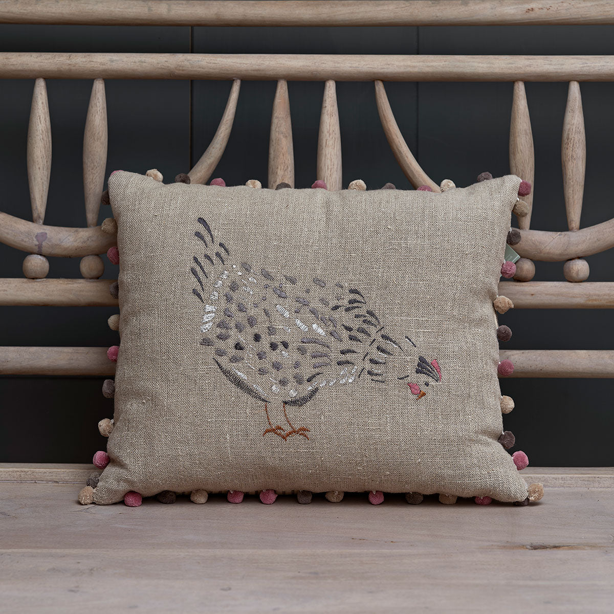 Embroidered black hen linen cushion on a rustic wooden bench seat