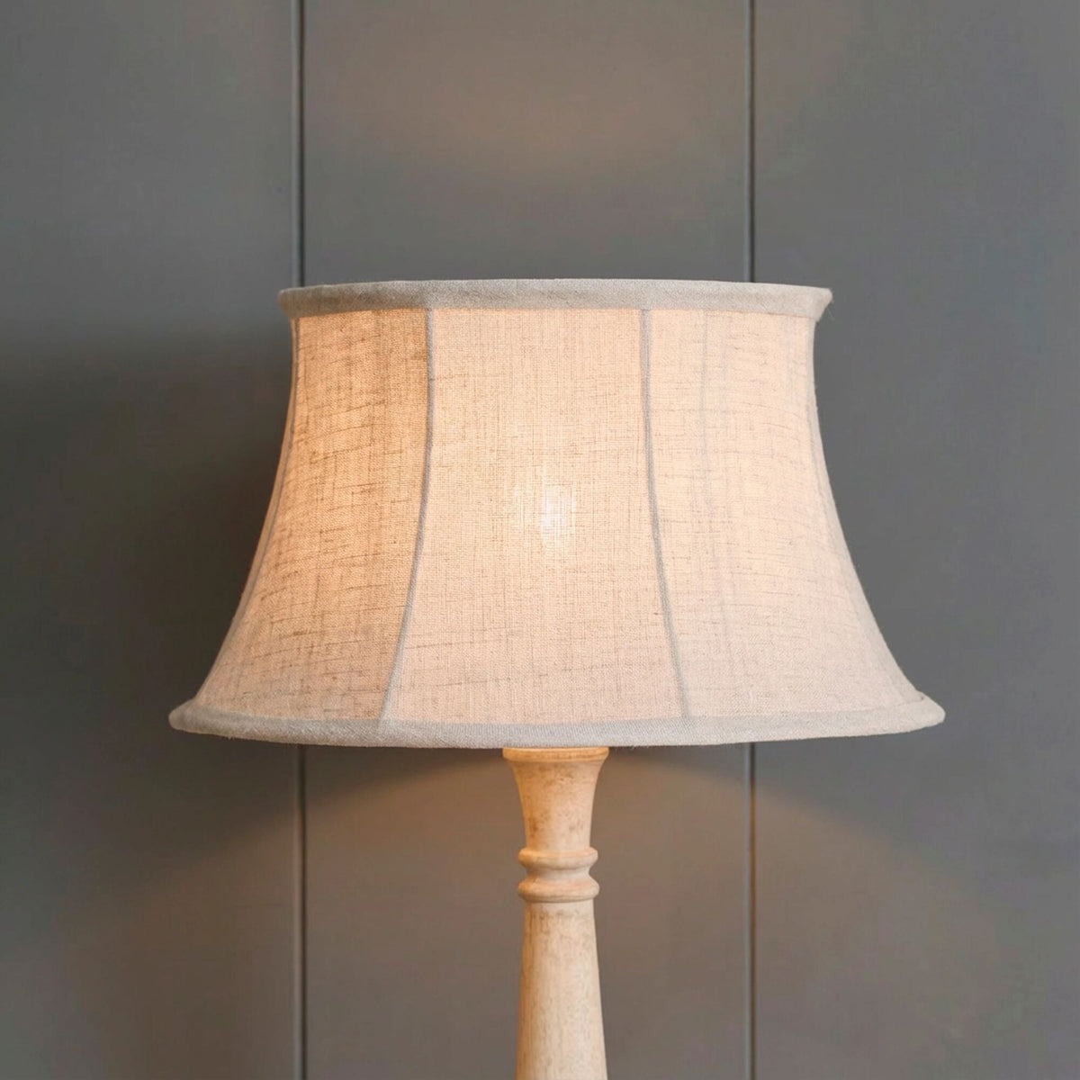 Natural linen framed lampshade lit and glowing warmly on a turned wooden base