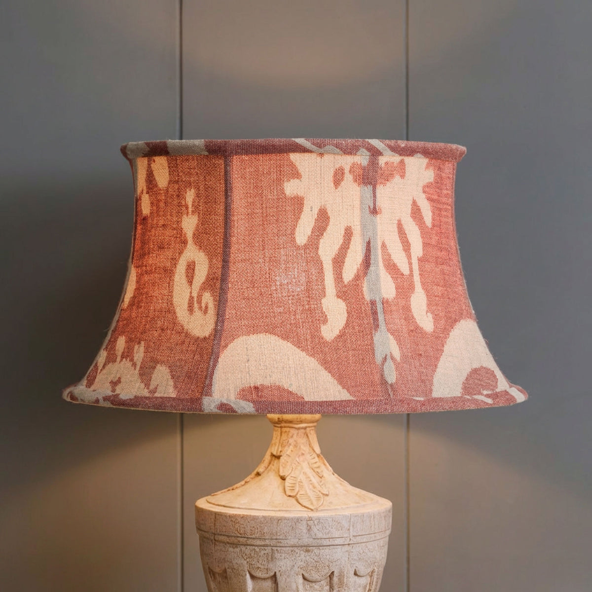 Lit Red Sacha framed lampshade glowing above a carved wooden base