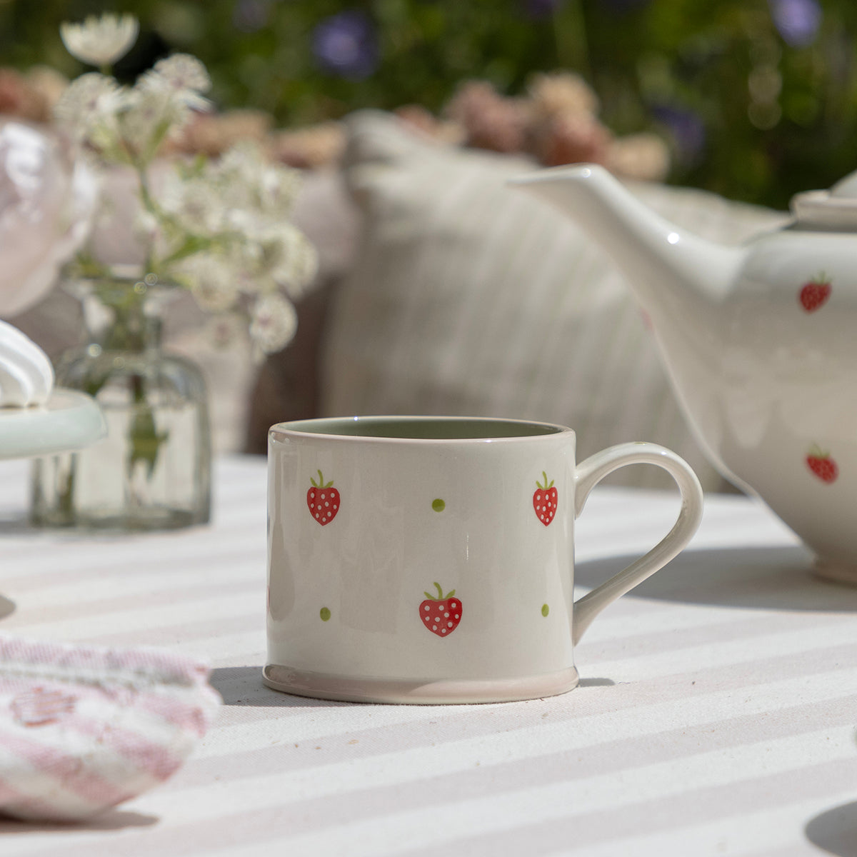 Strawberry mugs on a garden table beside a jug of flowers