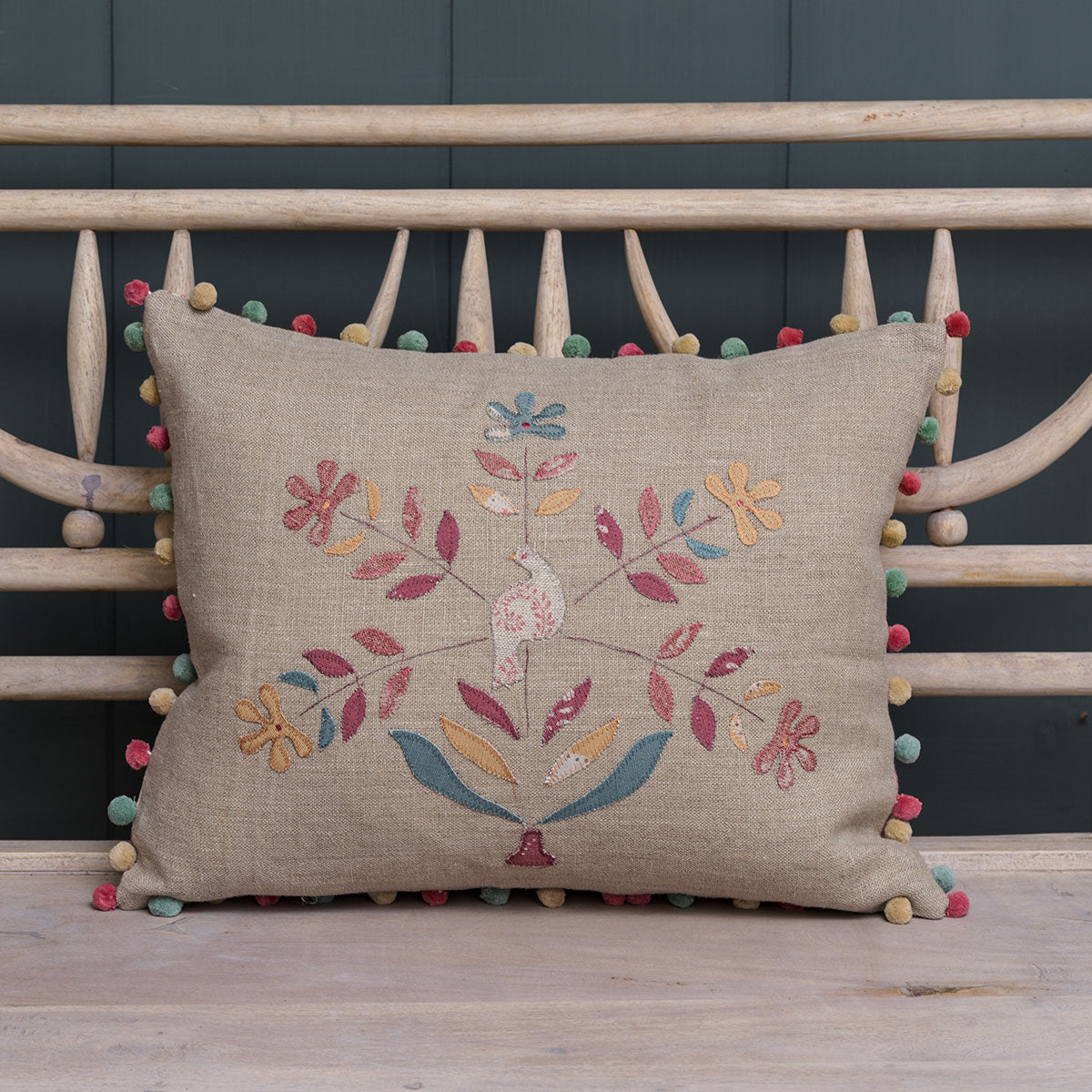Bird in Daisy Tree cushion with pom pom trim on a bench