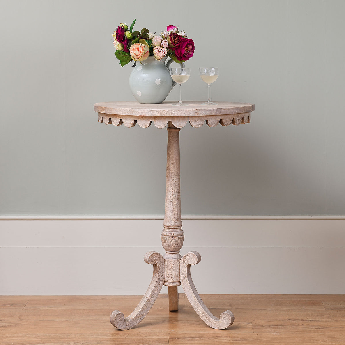 Scallop-edged bistro table with a posy of roses against a pale wall