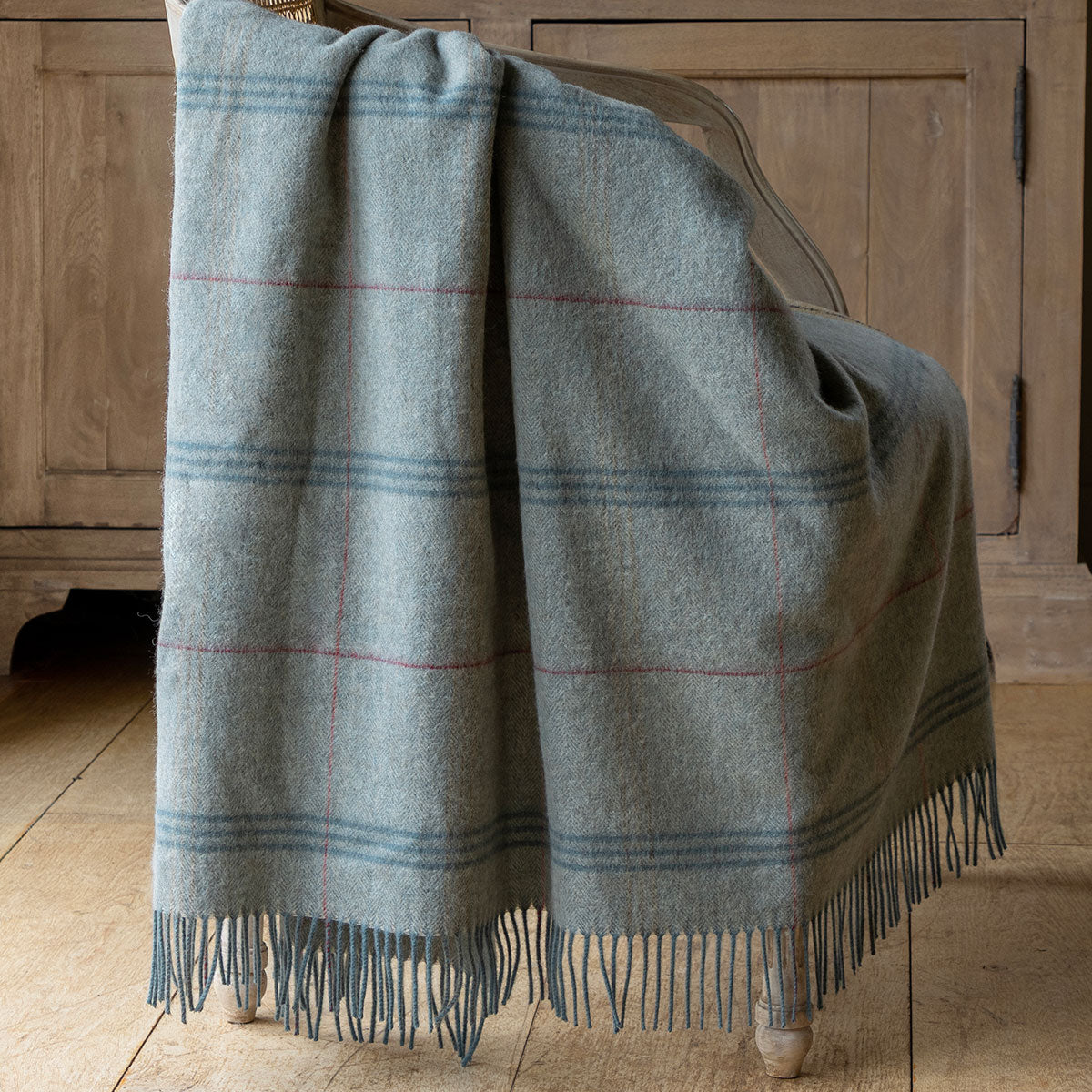 Blue Haze tartan lambswool throw draped over an oak chest with fringing
