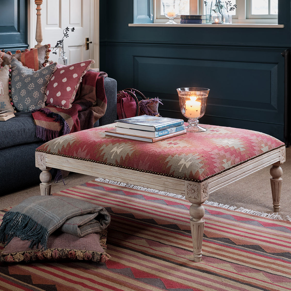 Kilim footstool used as a table beside a sofa in a blue panelled room