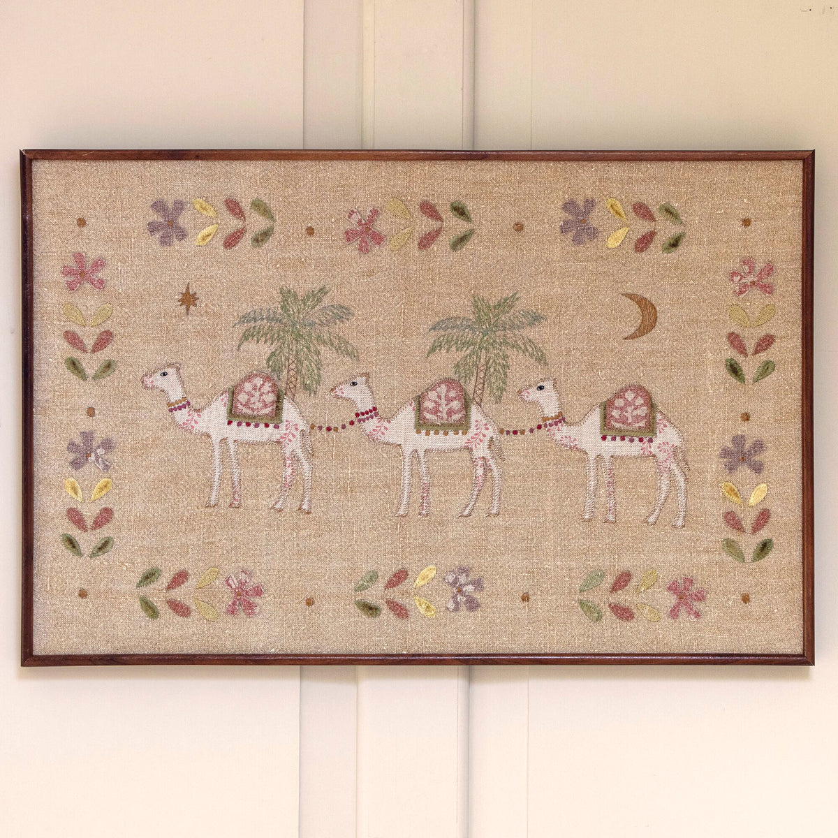 Embroidered camel train wall hanging in a mango wood frame on panelling