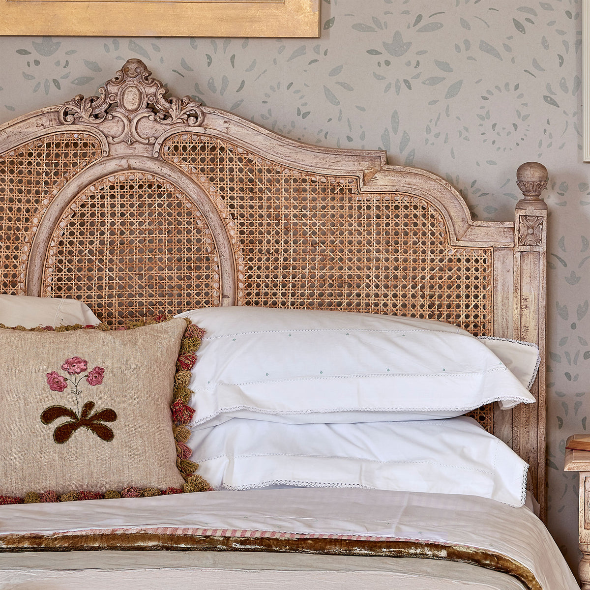 Carved caned Gustavian headboard with embroidered cushions and white pillows