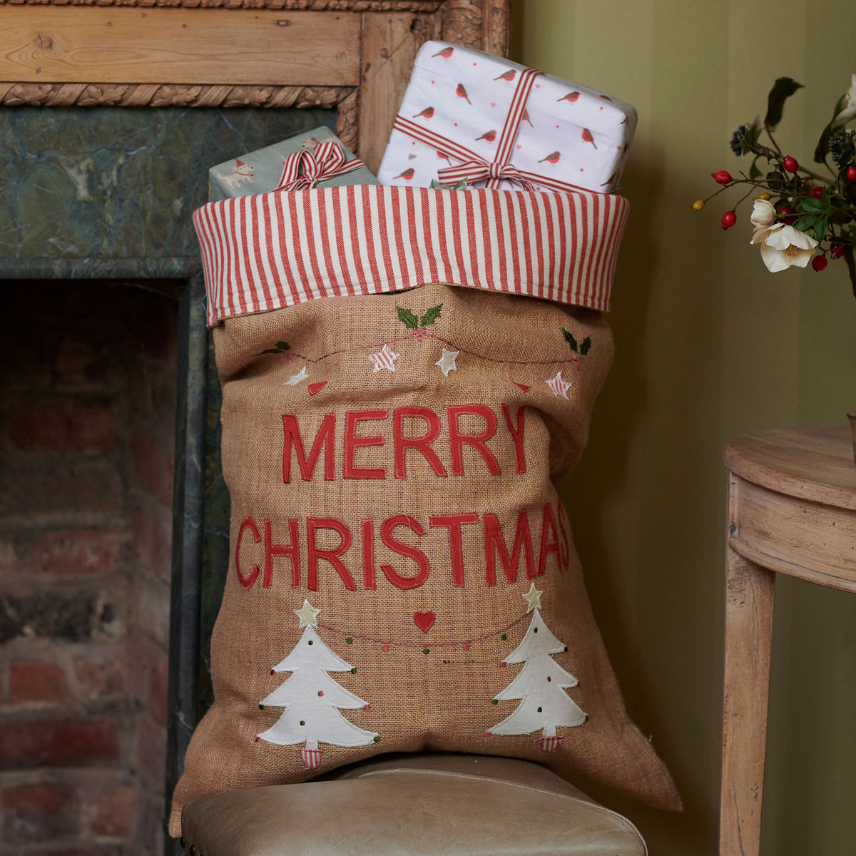 Hessian Christmas sack with appliqued trees at a brick fireplace