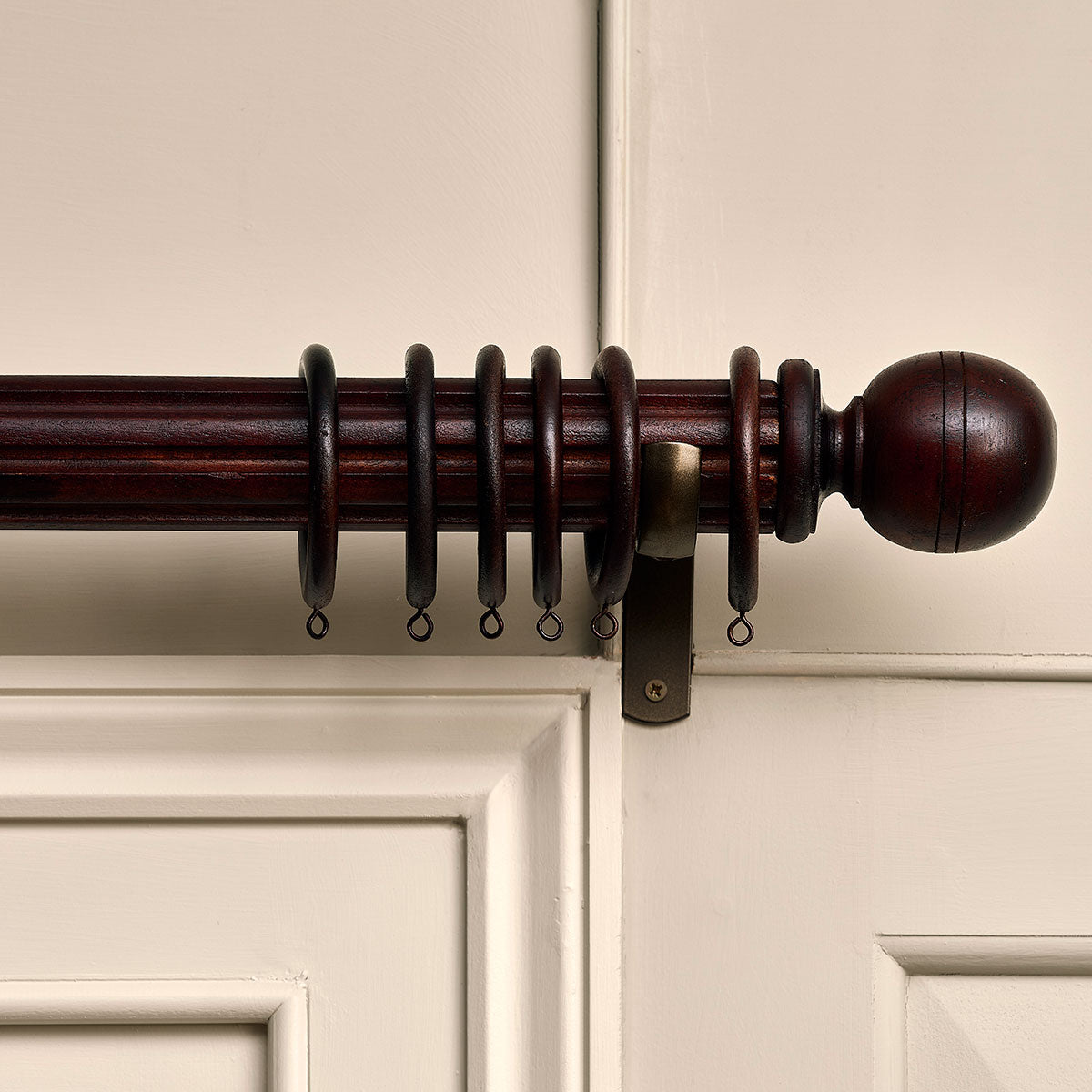 Dark wood reeded curtain pole with rings and ball finial on panelling