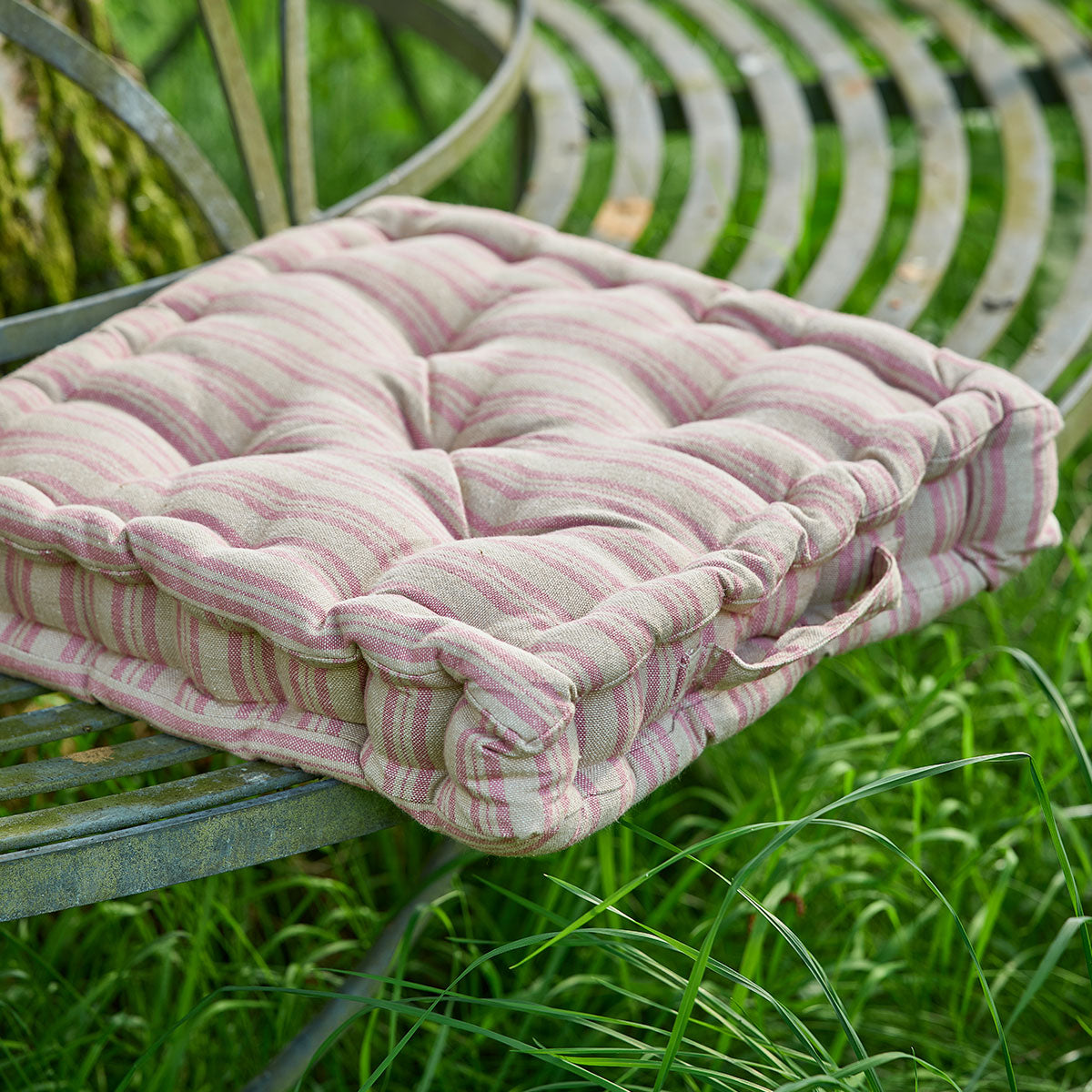 Dusky pink ticking stripe box cushion on a curved garden bench