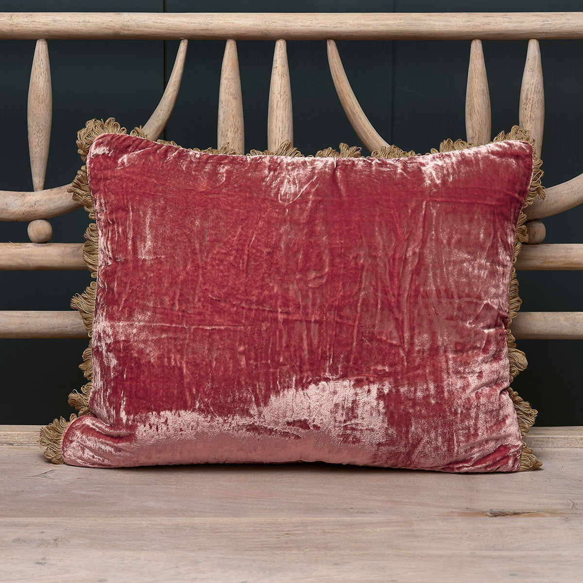 Dusky rose crushed velvet cushion with tassel trim on a painted bench