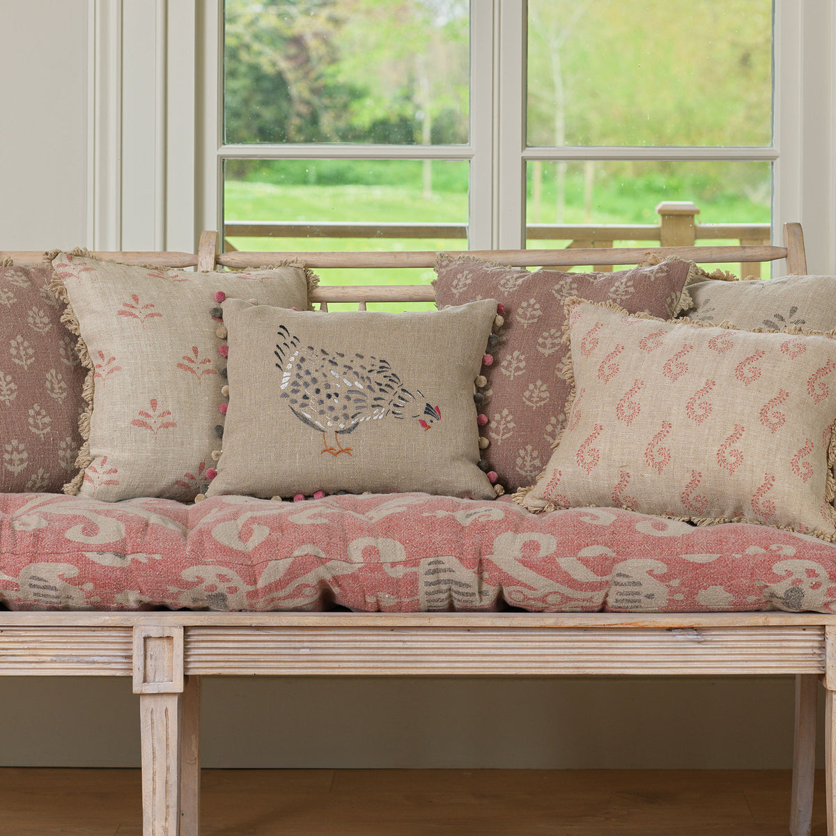 Black hen cushion among pink cushions along a long window seat
