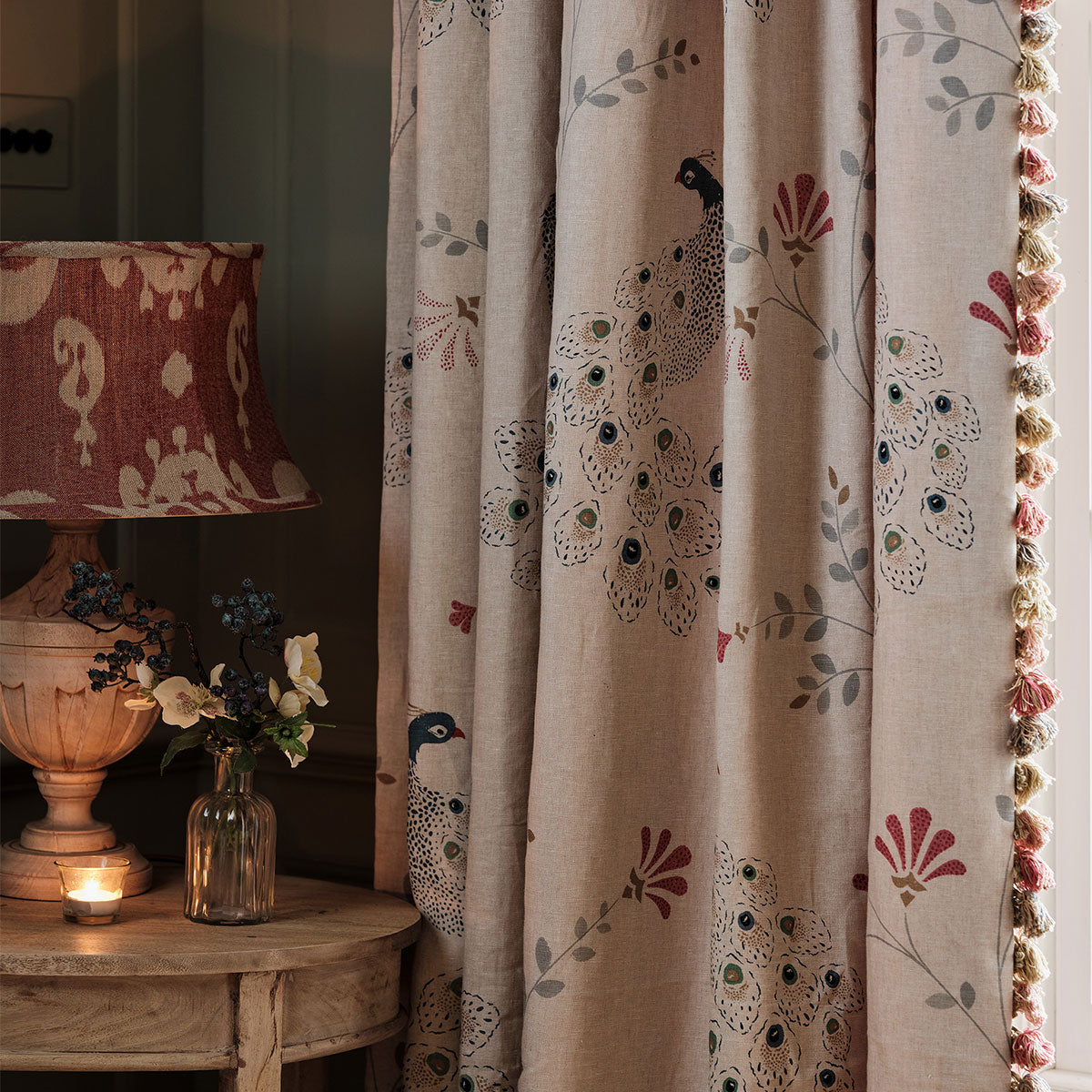 Peacock printed linen curtain beside a lit lamp and candlelight at a corner table