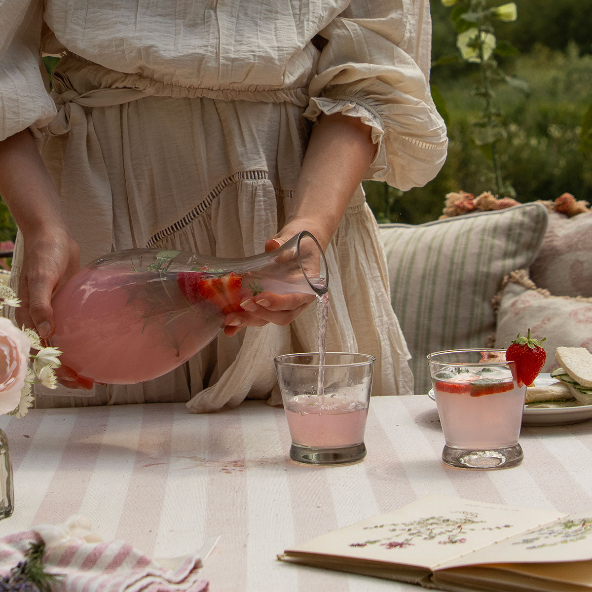 Pouring pink cordial into a hand-blown tumbler at an outdoor table