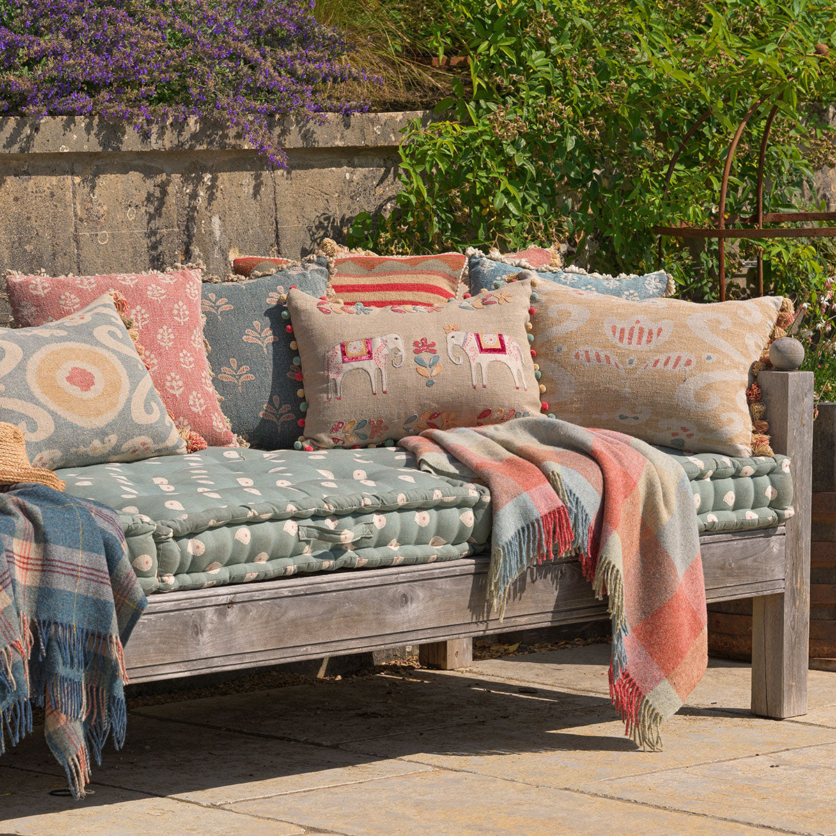 Embroidered elephant cushion among cushions on a stone garden daybed