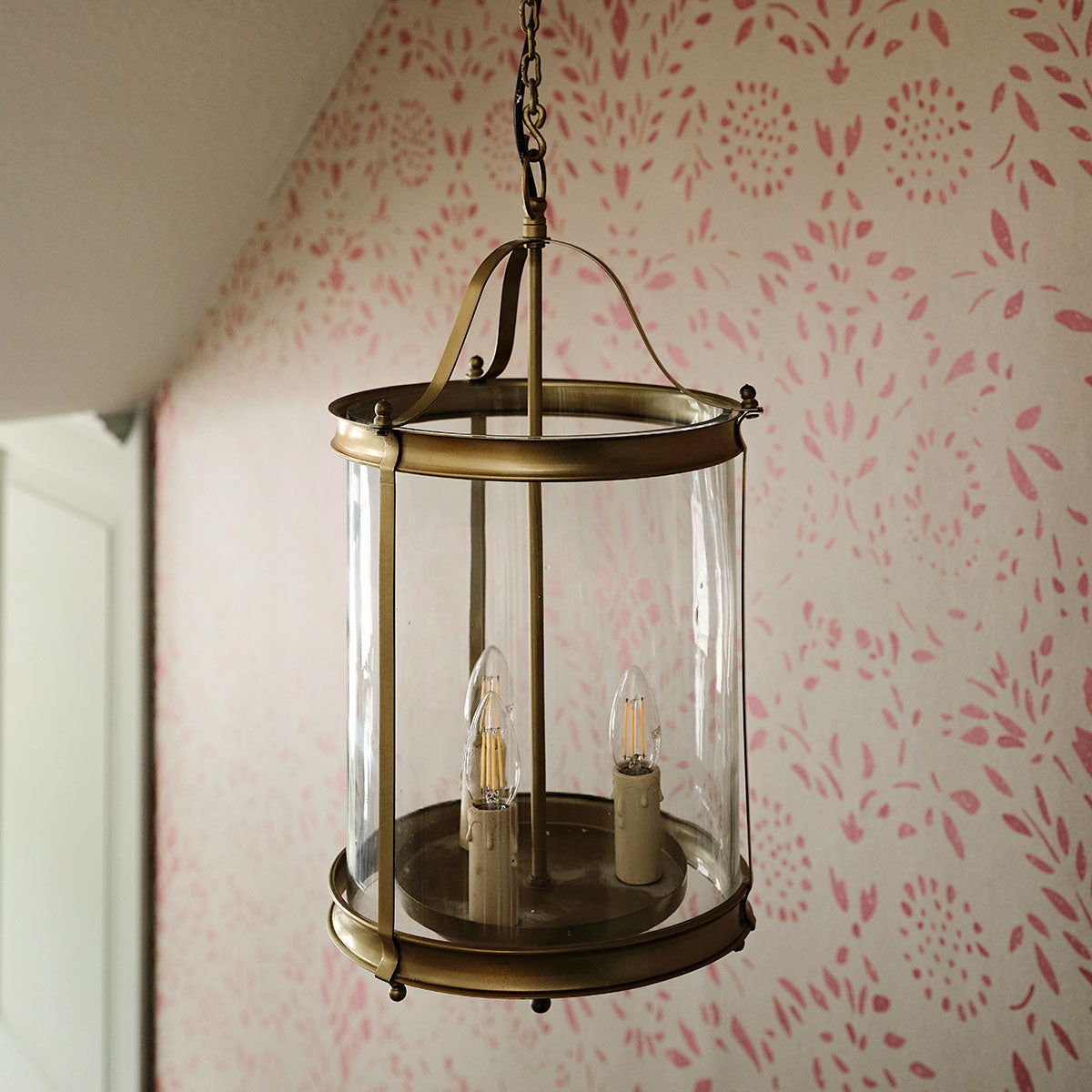 Brass lantern lit by candles on a landing with printed wallpaper