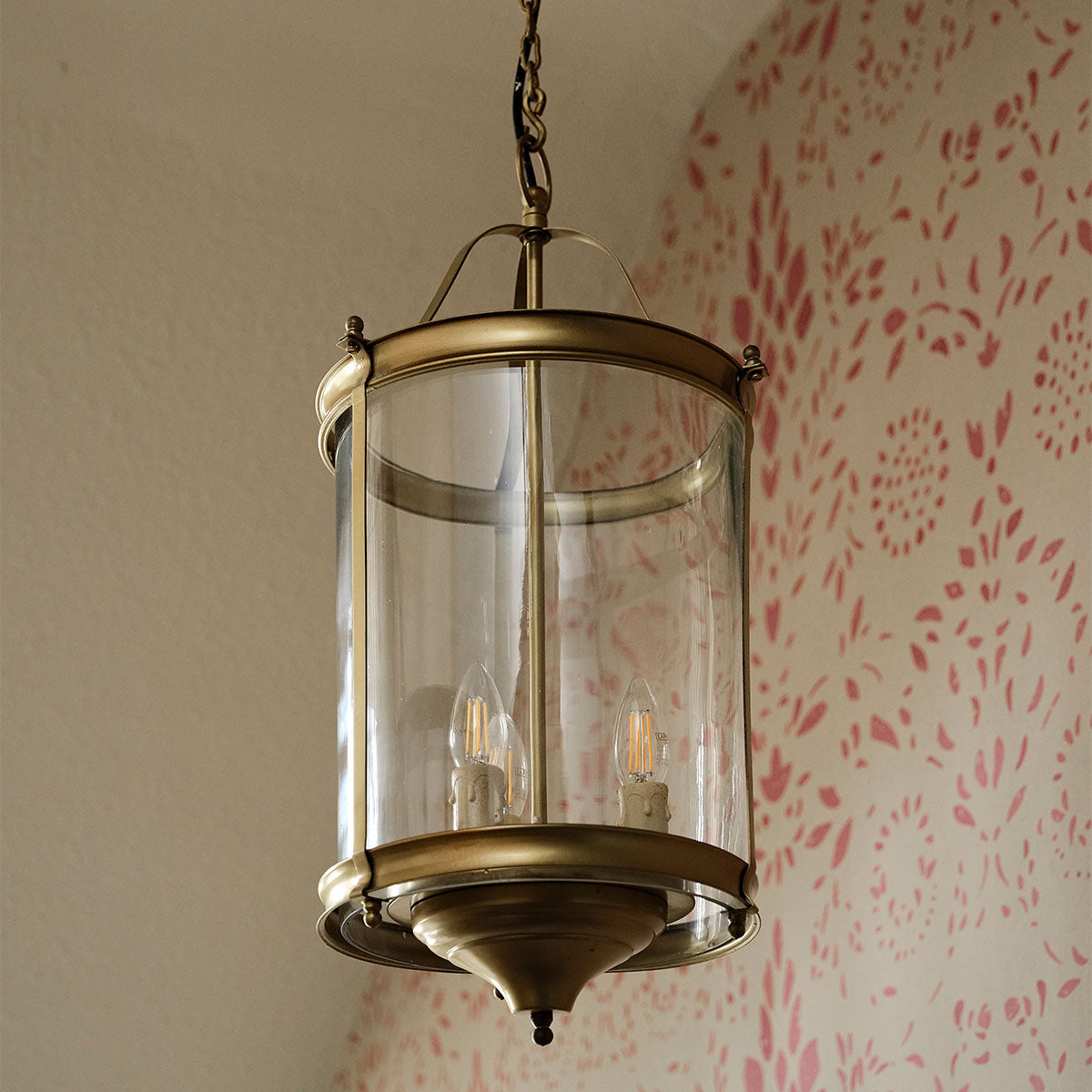 Brass lantern with glass panes hanging against pink patterned wallpaper
