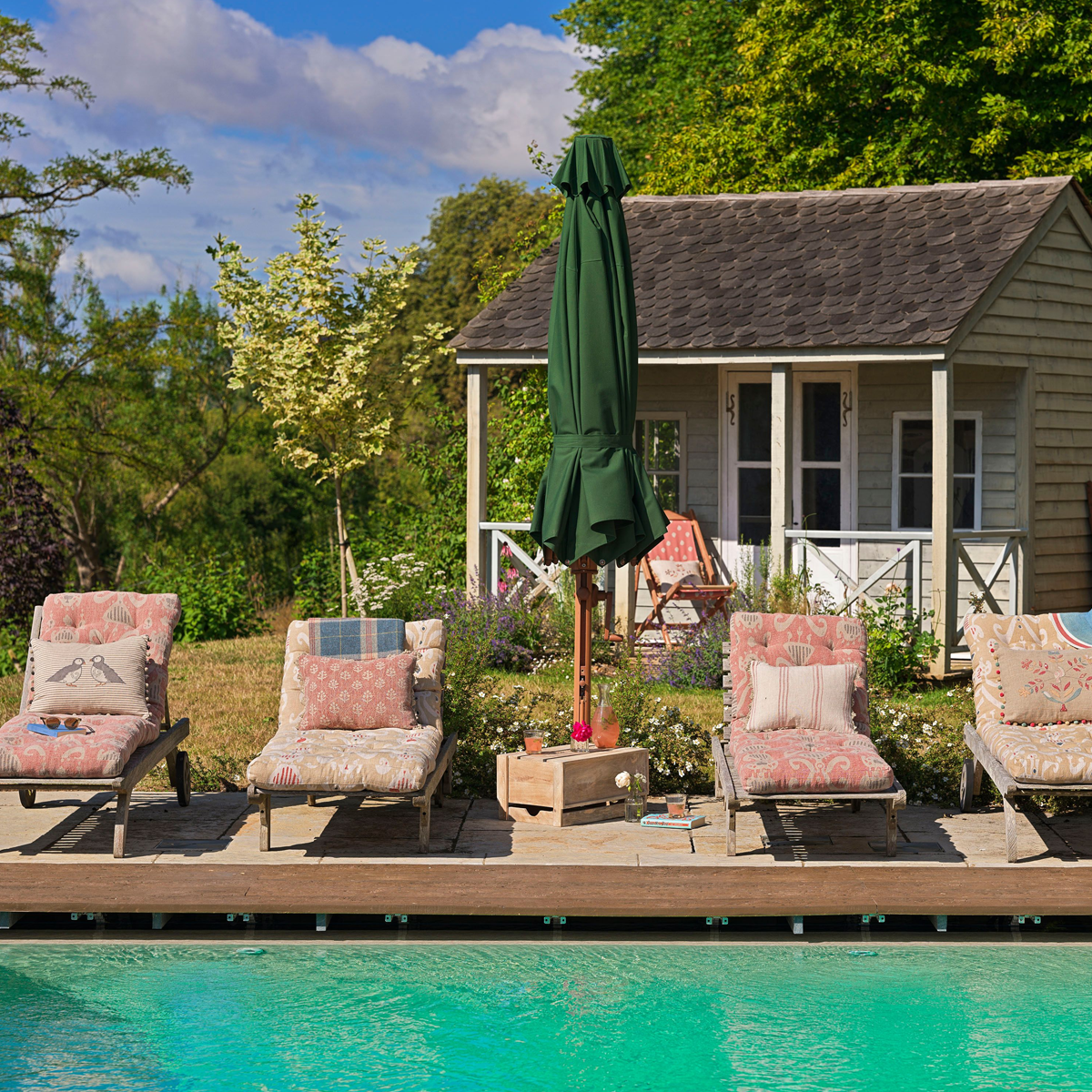 Cushioned loungers beside a swimming pool with a green parasol