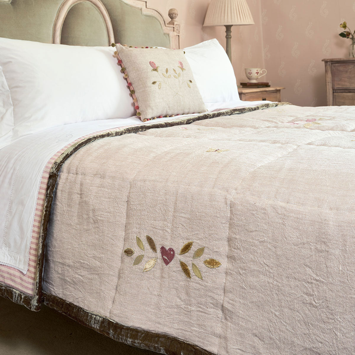Rose rustic linen quilt folded across a bed with pink ticking bolster