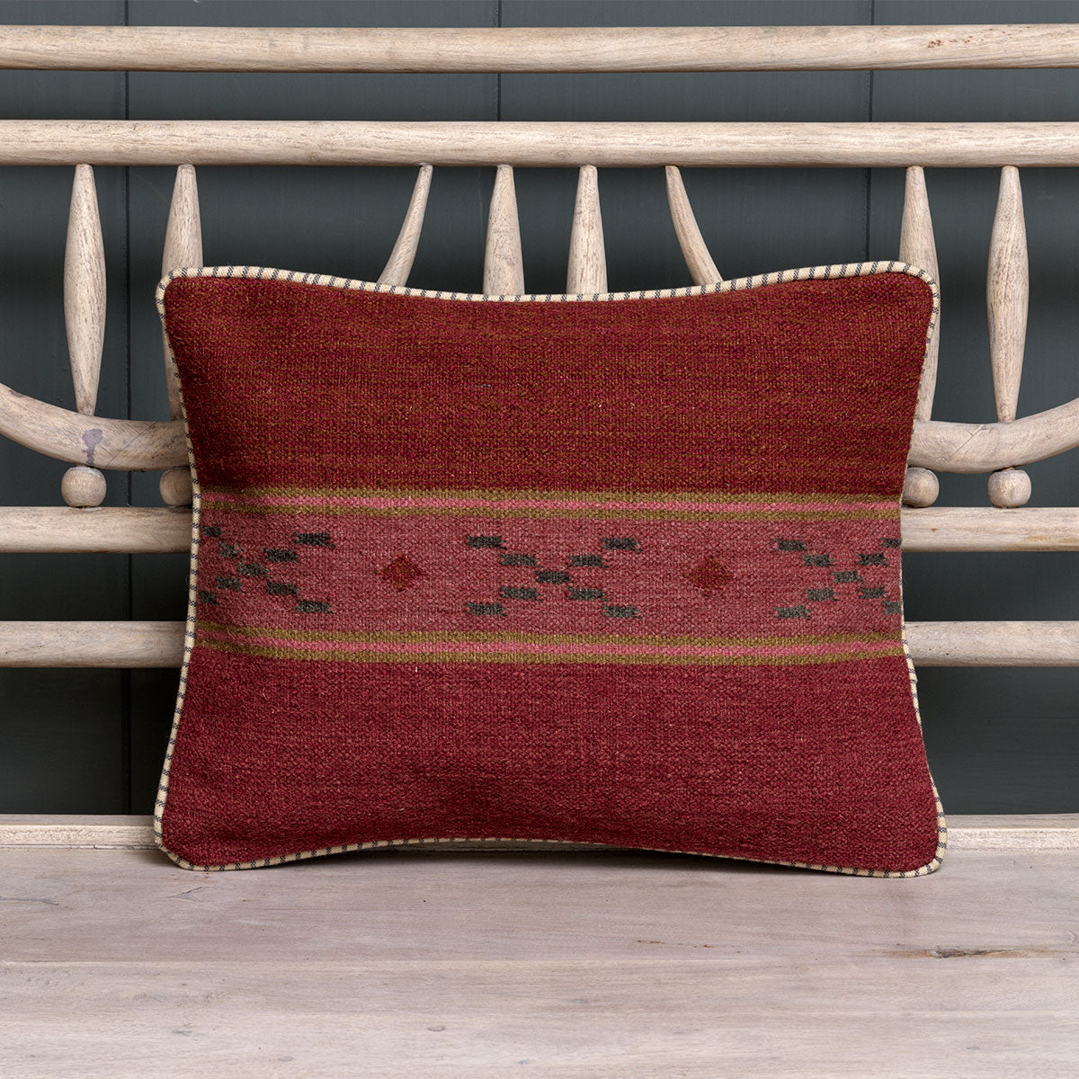 Small russet striped kilim cushion on a dark blue slatted bench