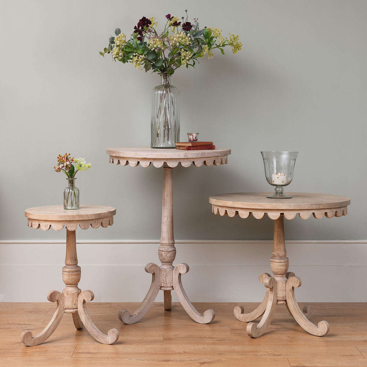 Two tiny scalloped side tables at different heights against a pale wall