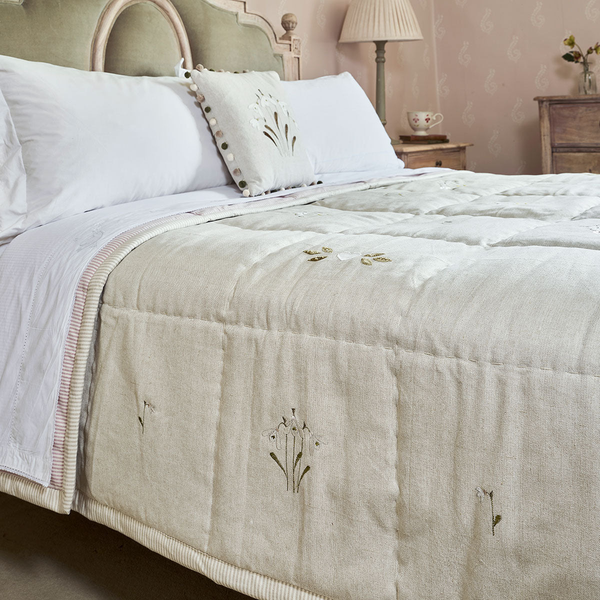Snowdrop dove grey cotton quilt with embroidered snowdrops on a bed
