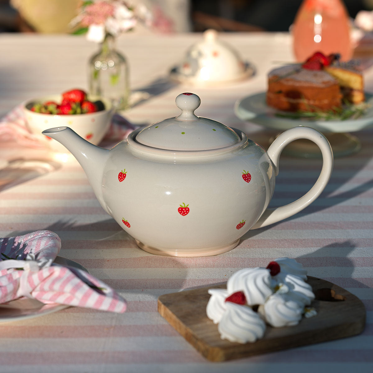 Strawberry giant teapot with meringues and cakes on a striped cloth