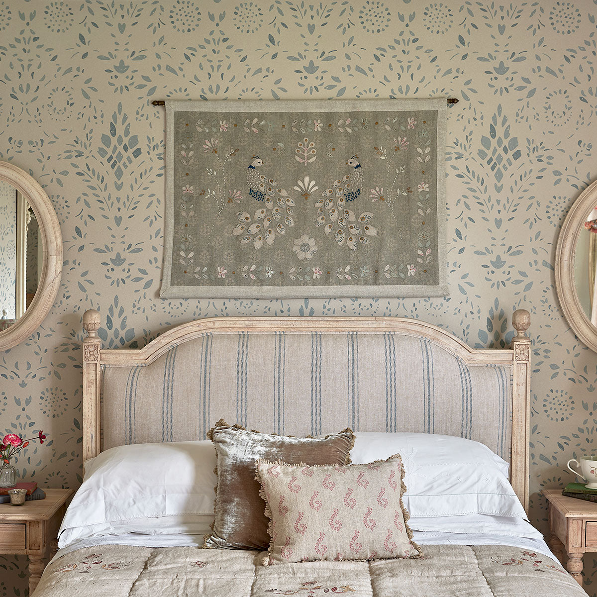 Peacock wall hanging above a bed in a wallpapered bedroom
