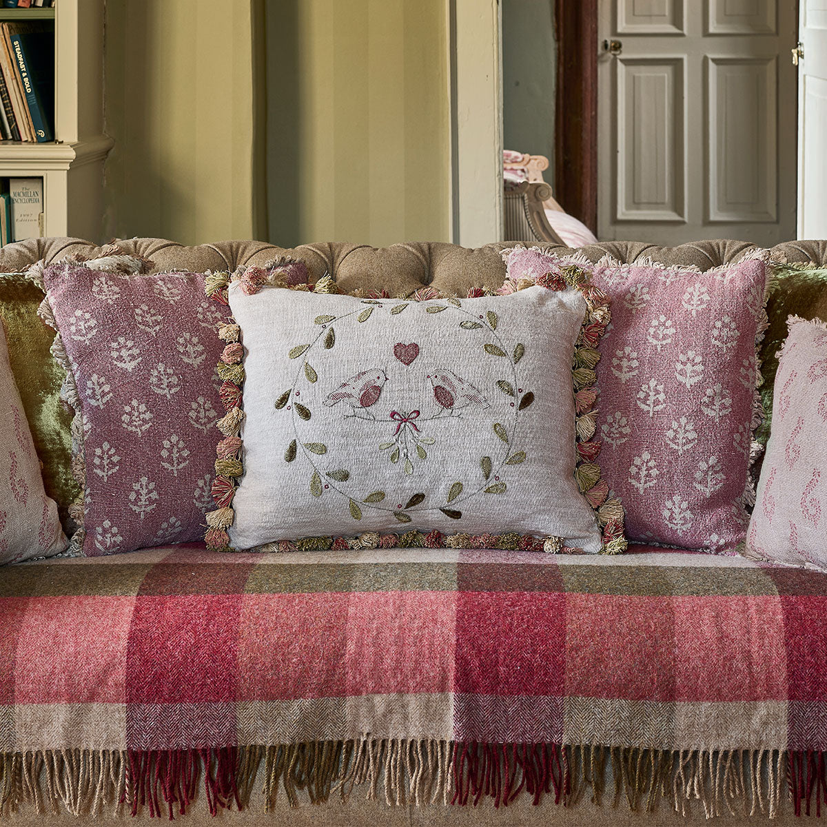 Winter robins cushion among pink cushions on a sofa with a red check throw