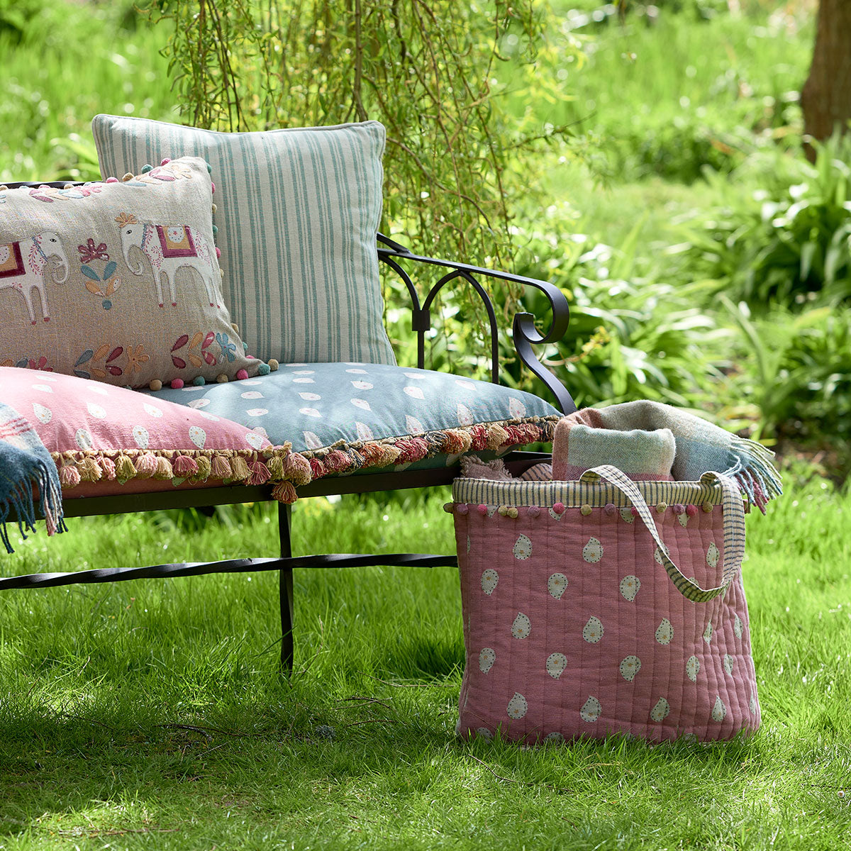 Rose Mika beach bag on the lawn beside a cushioned garden bench