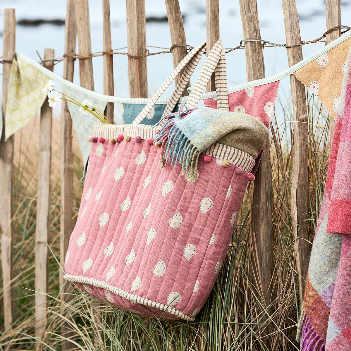 Rose Mika beach bag with pom poms hanging on a bamboo screen