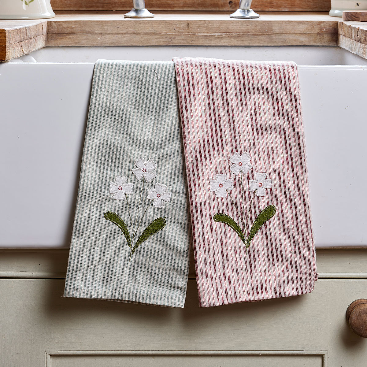 Pair of embroidered flower tea towels hanging on a rail above a range