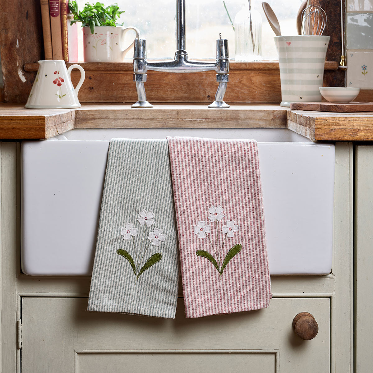 Green and pink striped embroidered tea towels hung beside a Belfast sink