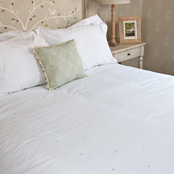 Bed made up in duck egg spot bedding with a green cushion