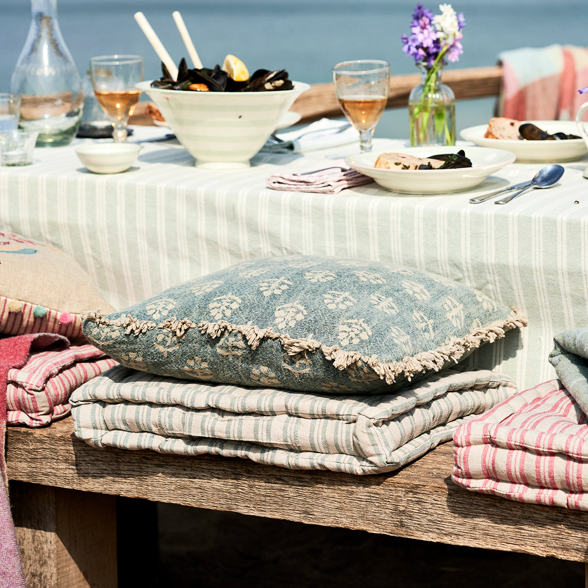 Box cushions on a bench beside a seaside table of shellfish