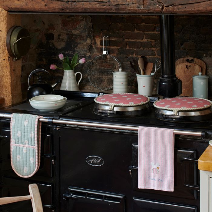 Black Aga in a brick alcove with rose lid covers and oven gloves