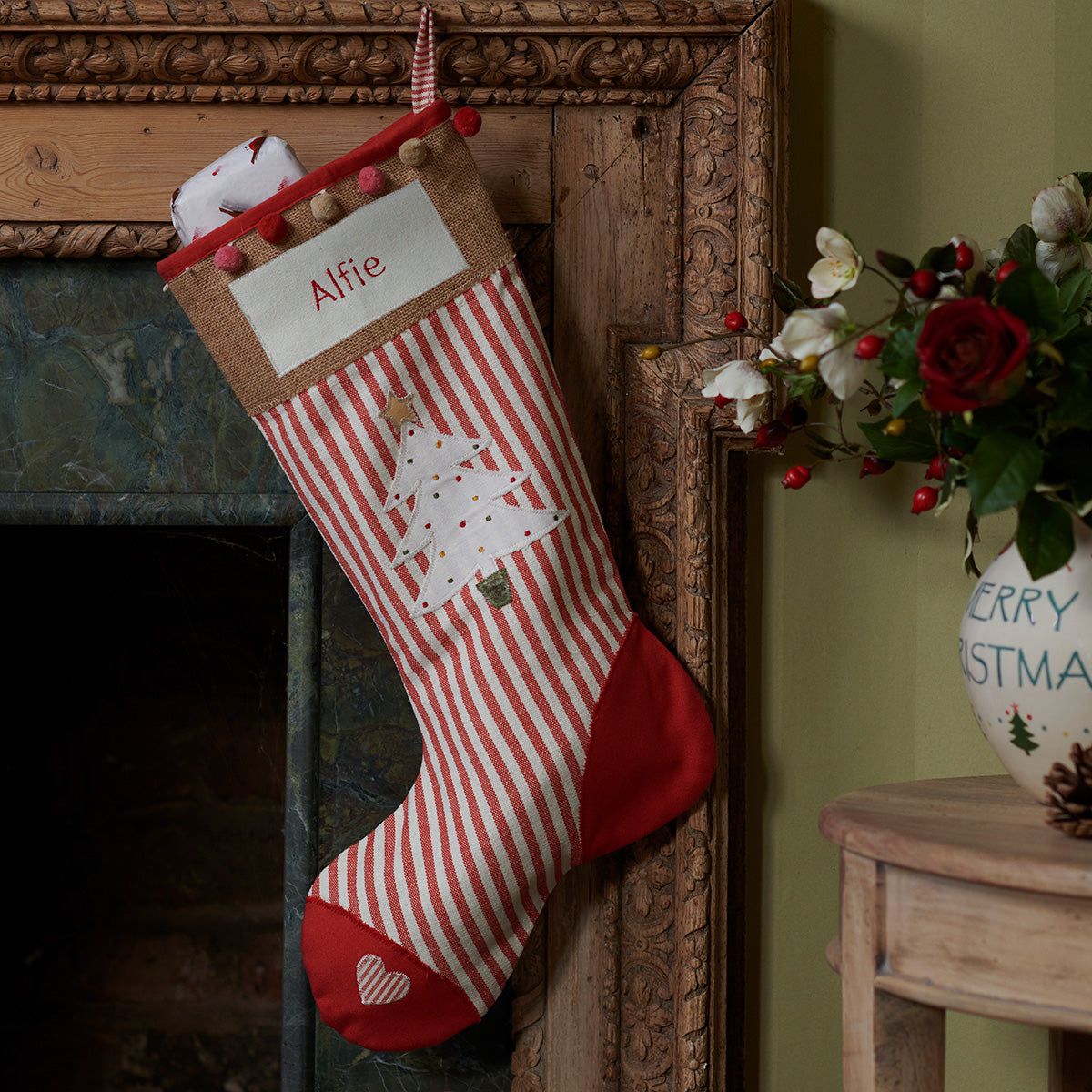 Personalised Christmas tree stocking hung at a fireplace with winter foliage
