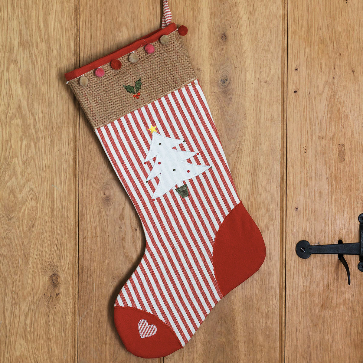 Red striped Christmas stocking with applique tree hanging on a plank door