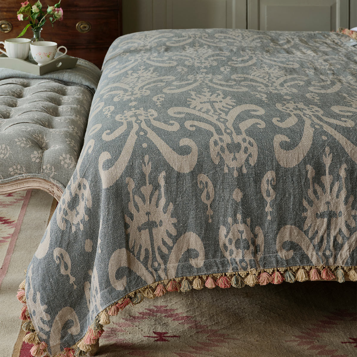 Tasselled linen throw spread across a buttoned bed, pom pom hem visible